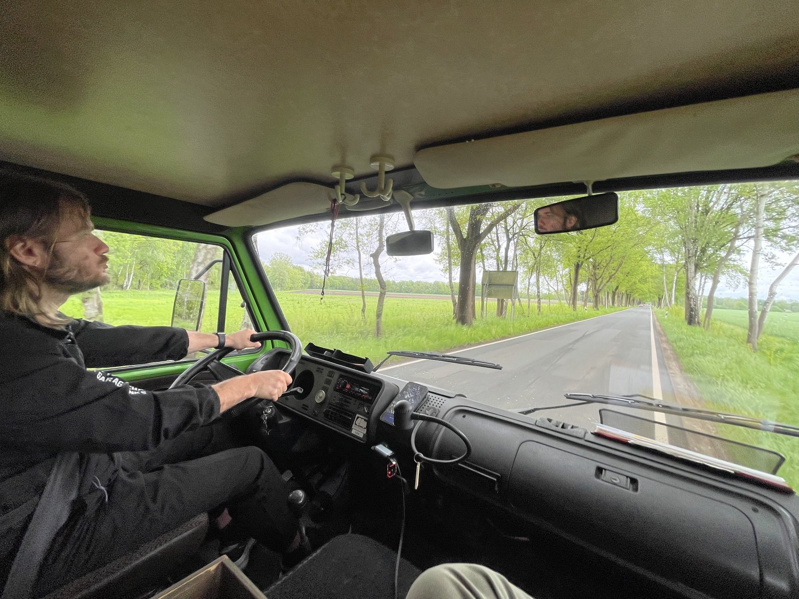 Driving the green VW LT28 Westfalia campervan along a tree-lined road in spring